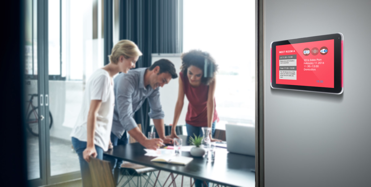 A meeting room with professionals having a discussion, a LV-Tron display showing the meeting room status is nearby