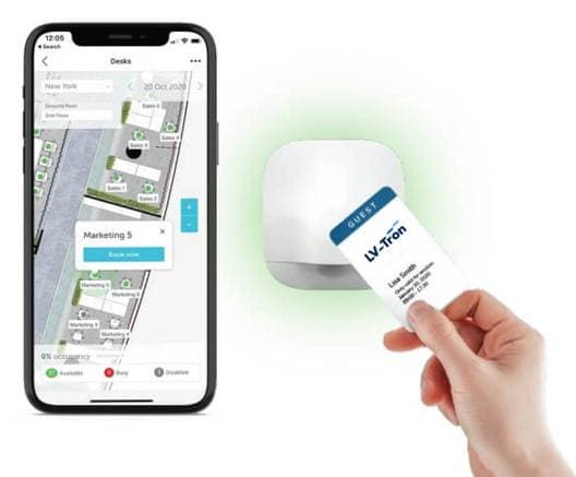 An image of a mobile phone showing an office floor plan and a hand holding an RFID card. The hand is placing the card on top of a desk booking device